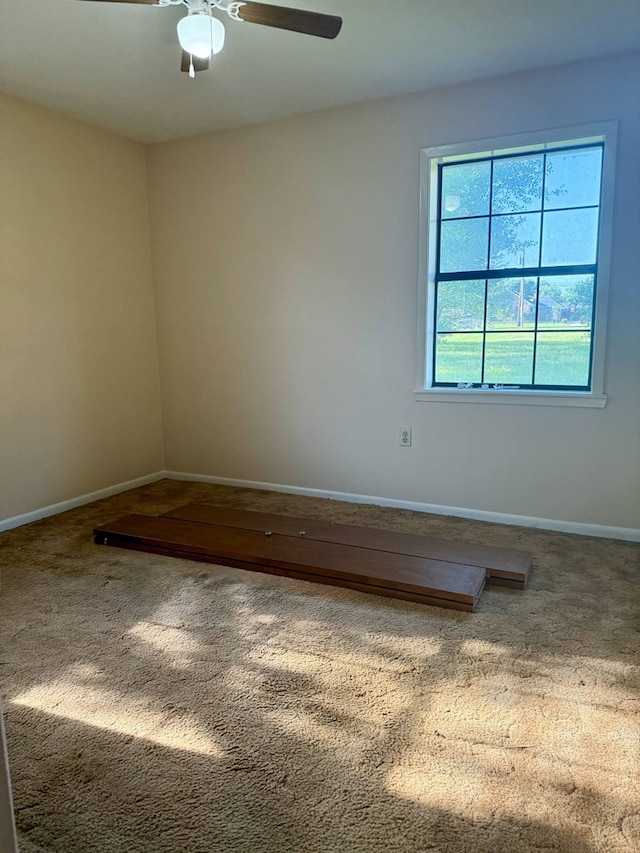 carpeted spare room featuring baseboards and a ceiling fan