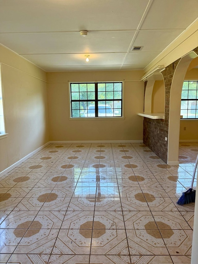 spare room featuring light tile patterned floors, arched walkways, visible vents, and baseboards