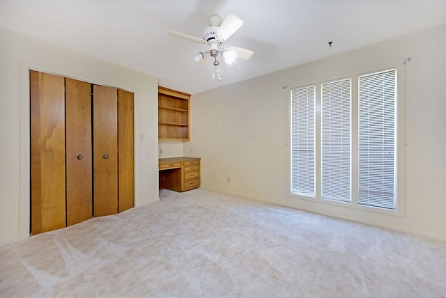 unfurnished bedroom with ceiling fan, light colored carpet, built in desk, and a closet