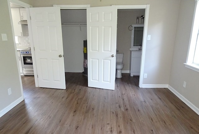 unfurnished bedroom featuring sink, water heater, wood-type flooring, connected bathroom, and a closet