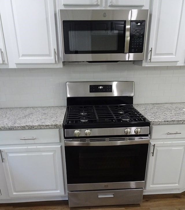 kitchen featuring decorative backsplash, light stone countertops, white cabinets, and stainless steel appliances