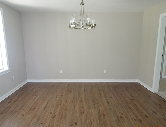 spare room featuring dark wood-type flooring and a chandelier