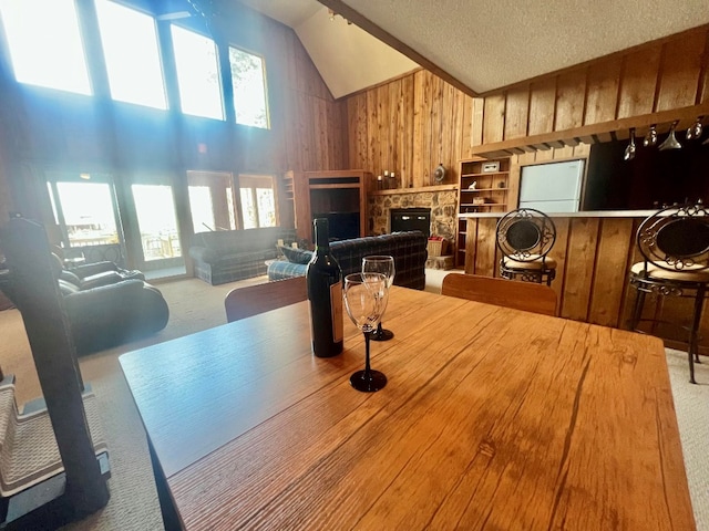 dining room featuring high vaulted ceiling, a textured ceiling, carpet floors, wooden walls, and a fireplace