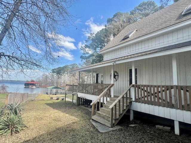 entrance to property featuring a water view, a lawn, roof with shingles, and fence