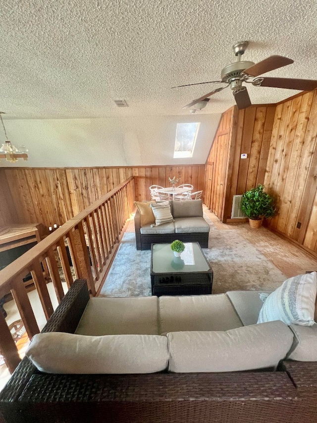 living room with a textured ceiling, wooden walls, a skylight, carpet flooring, and ceiling fan