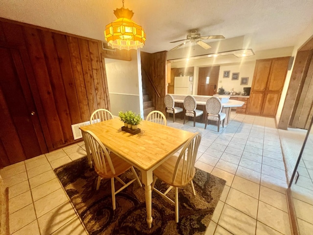 dining room featuring light tile patterned flooring, wood walls, stairs, and ceiling fan