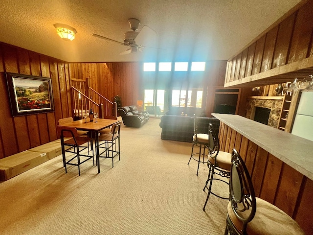 interior space featuring a textured ceiling, carpet, wood walls, ceiling fan, and stairs