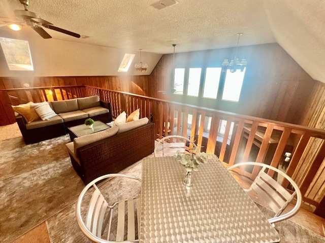 interior space with wooden walls, visible vents, lofted ceiling, ceiling fan with notable chandelier, and a textured ceiling