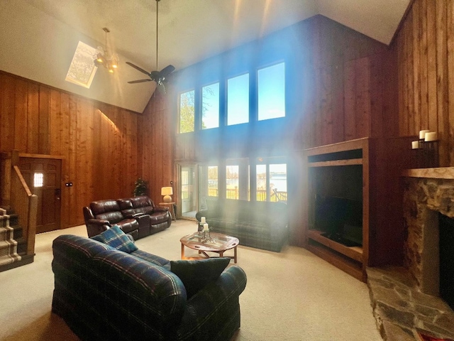 carpeted living room featuring stairway, wood walls, a fireplace, high vaulted ceiling, and a ceiling fan