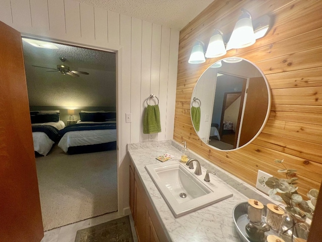 ensuite bathroom featuring vanity, wooden walls, ceiling fan, a textured ceiling, and connected bathroom