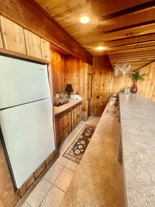 kitchen with wooden walls, light tile patterned flooring, wood ceiling, and freestanding refrigerator