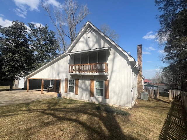 rear view of house with a balcony, fence, a yard, a chimney, and concrete driveway