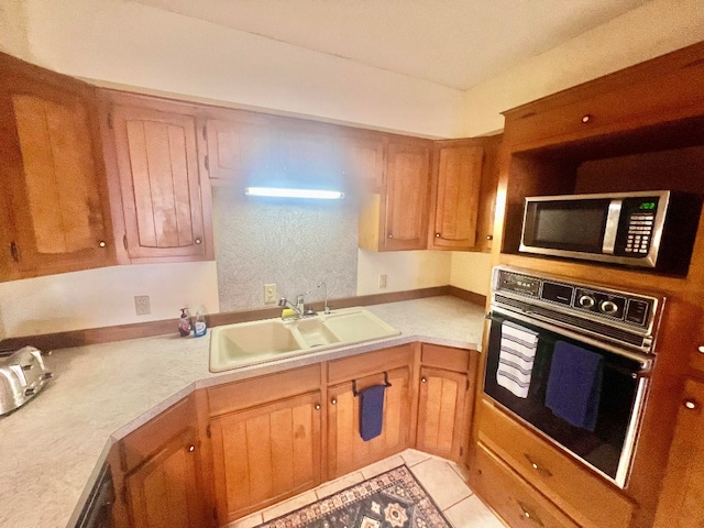 kitchen featuring light tile patterned floors, a sink, oven, light countertops, and stainless steel microwave