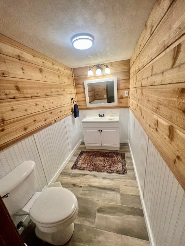 half bath with toilet, vanity, baseboards, and wood finished floors