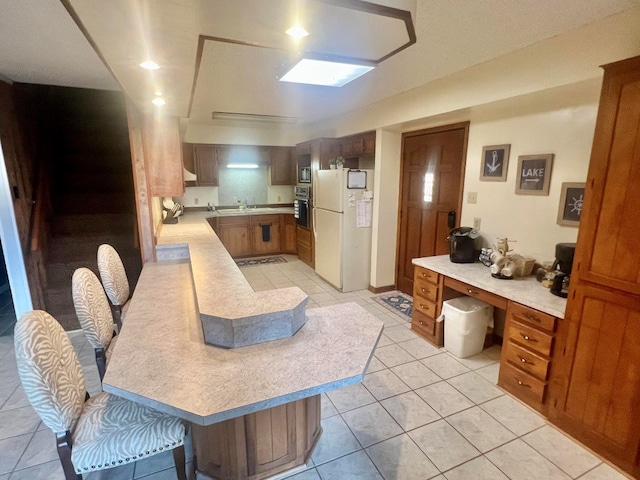 kitchen featuring light tile patterned floors, freestanding refrigerator, a sink, oven, and light countertops