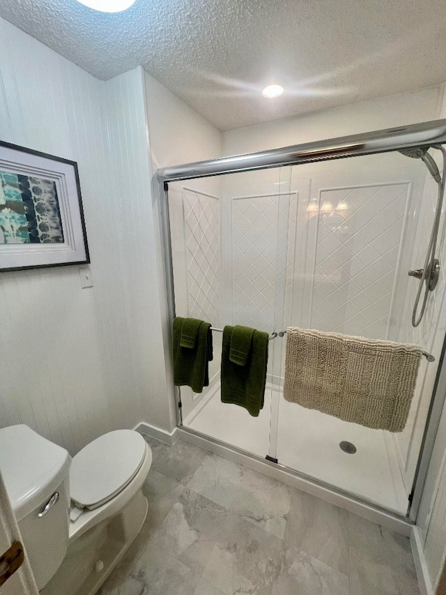 full bathroom featuring toilet, marble finish floor, a stall shower, and a textured ceiling