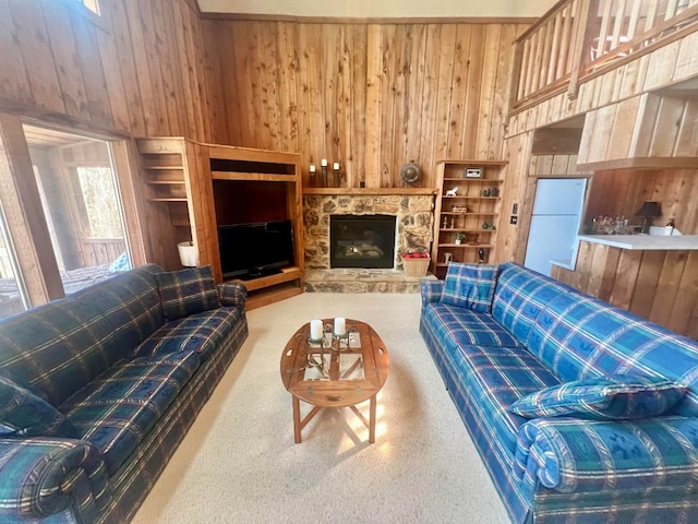living room with carpet floors, wooden walls, and a stone fireplace