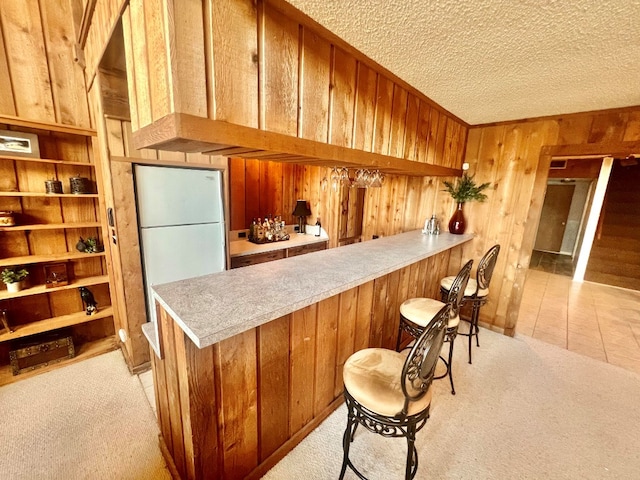 bar featuring freestanding refrigerator, bar area, light colored carpet, and wood walls