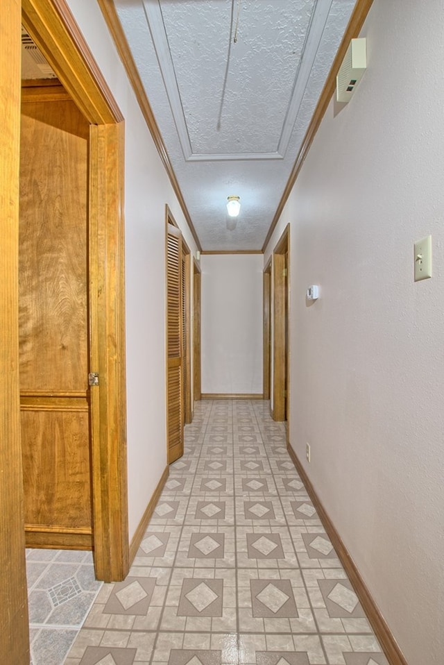 corridor with ornamental molding, a textured ceiling, and light tile patterned floors