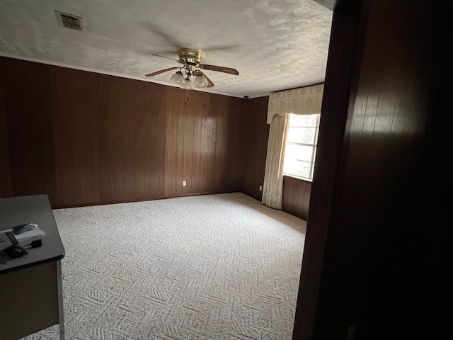 unfurnished room featuring visible vents, a textured ceiling, wooden walls, carpet flooring, and ceiling fan