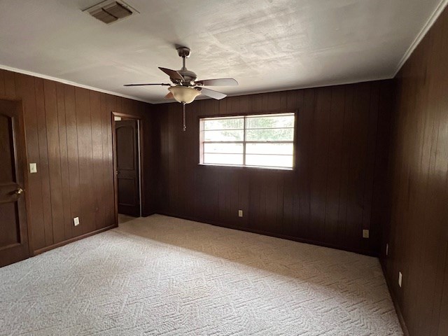 unfurnished room featuring visible vents, ornamental molding, wood walls, light colored carpet, and ceiling fan