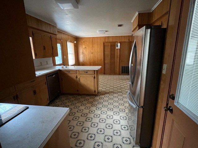 kitchen with freestanding refrigerator, a peninsula, wood walls, light countertops, and dishwasher