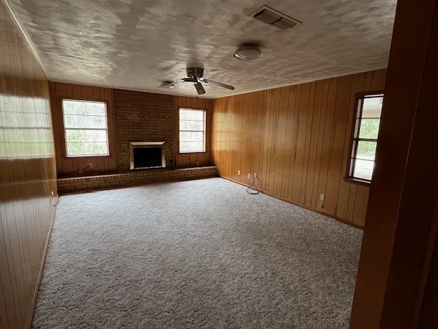 unfurnished living room with wooden walls, visible vents, a brick fireplace, carpet, and a textured ceiling