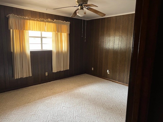 empty room with light carpet, wooden walls, crown molding, and a ceiling fan