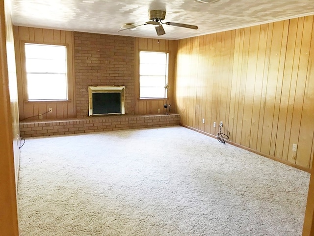 unfurnished living room featuring carpet flooring, a ceiling fan, wood walls, and a wealth of natural light