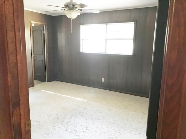 carpeted spare room with wood walls and ceiling fan