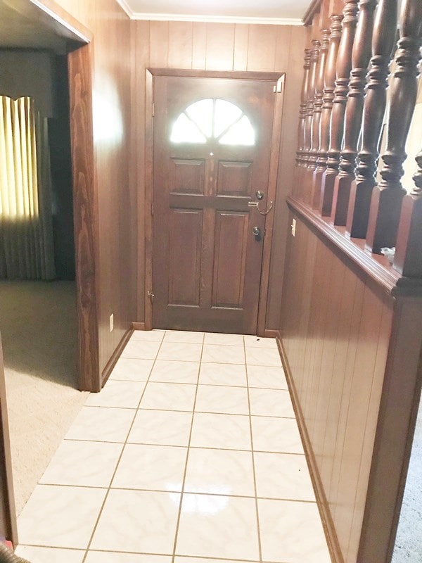 interior space with light tile patterned floors, wood walls, and ornamental molding