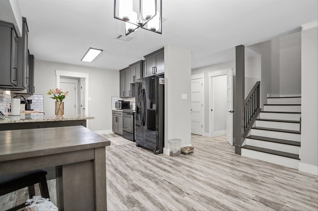 kitchen featuring gray cabinets, backsplash, light stone counters, black appliances, and light wood-type flooring