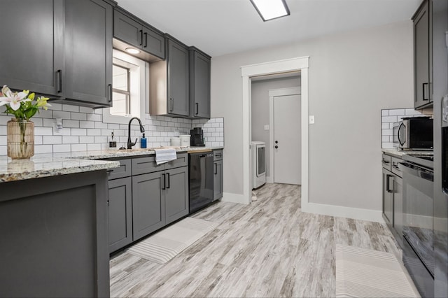 kitchen featuring gray cabinetry, light hardwood / wood-style flooring, black dishwasher, light stone countertops, and decorative backsplash