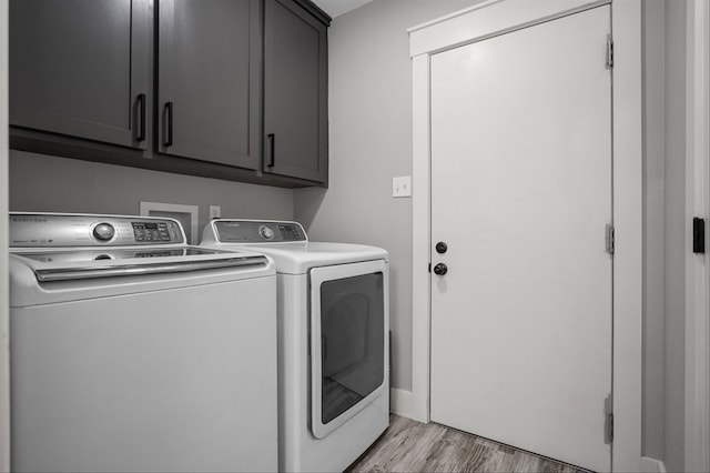 clothes washing area with cabinets, washing machine and dryer, and light hardwood / wood-style flooring