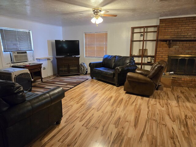 living room with ceiling fan, light hardwood / wood-style flooring, a textured ceiling, and a brick fireplace