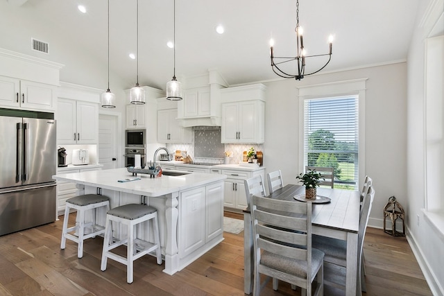 kitchen featuring decorative light fixtures, white cabinetry, a kitchen island with sink, and appliances with stainless steel finishes