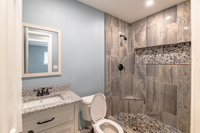 bathroom with a tile shower, vanity, and toilet