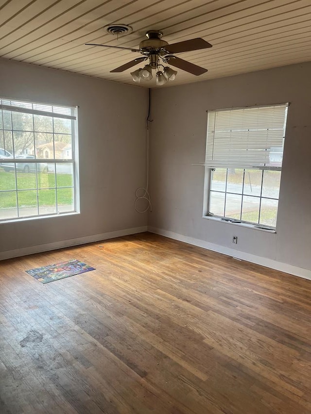 spare room with baseboards, ceiling fan, a healthy amount of sunlight, and wood finished floors