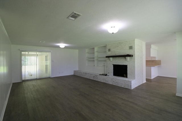 unfurnished living room with built in shelves, dark wood-type flooring, and a brick fireplace