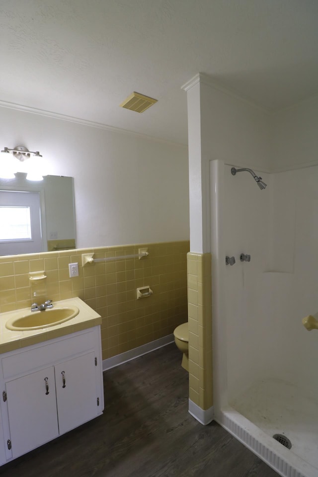 bathroom with a shower, hardwood / wood-style flooring, vanity, tile walls, and ornamental molding