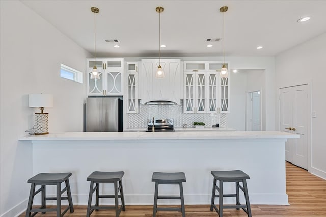 kitchen with glass insert cabinets, white cabinetry, appliances with stainless steel finishes, hanging light fixtures, and backsplash