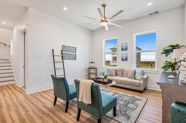 living area featuring visible vents, baseboards, ceiling fan, stairway, and light wood-style flooring