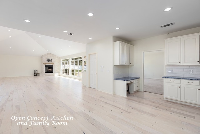 kitchen featuring a large fireplace, white cabinetry, light hardwood / wood-style flooring, and vaulted ceiling