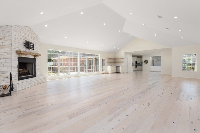 unfurnished living room featuring plenty of natural light, light hardwood / wood-style floors, a fireplace, and high vaulted ceiling