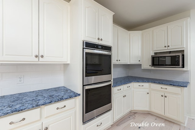 kitchen with white cabinetry, backsplash, dark stone counters, light hardwood / wood-style floors, and appliances with stainless steel finishes