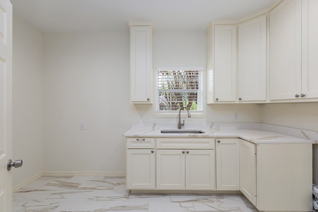 kitchen featuring light stone counters, sink, and white cabinets