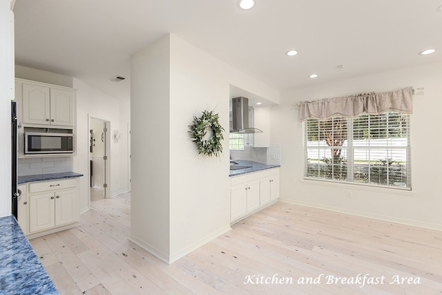 kitchen with tasteful backsplash, white cabinetry, light hardwood / wood-style floors, and wall chimney range hood