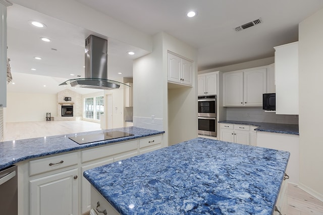 kitchen featuring white cabinets, black appliances, island range hood, and a fireplace