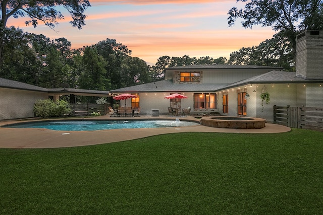 pool at dusk featuring an in ground hot tub, a patio, and a lawn