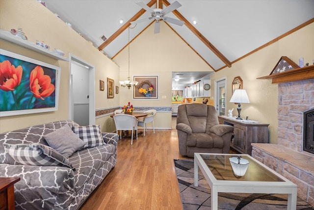 living room with ceiling fan with notable chandelier, a stone fireplace, wood-type flooring, and high vaulted ceiling